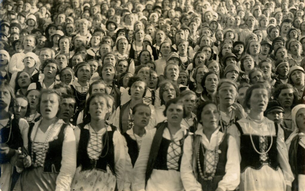 Senoje nuotraukoje dainuoja daugybė tautiniais kostiumais apsirengusios moterys ir merginos