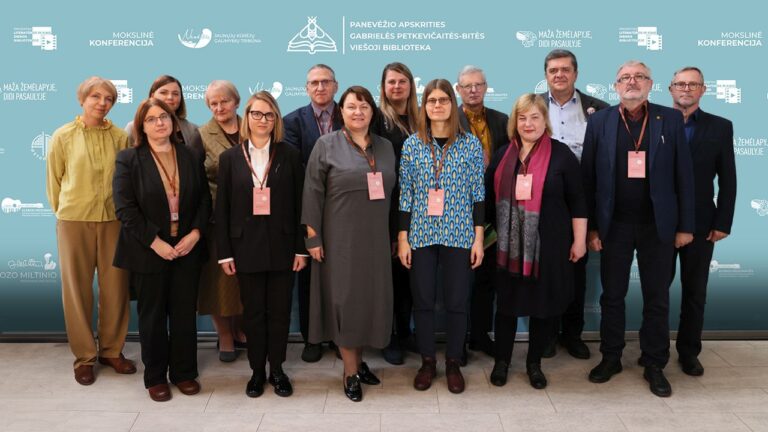 Grupė vyrų ir moterų konferencijos dalyvių stovi mėlynos foto sienelės fone