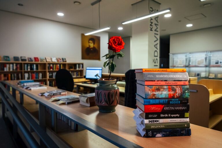 Didelė stirta knygų ant ilgo stalo bibliotekos knygų išdavimo erdvėje