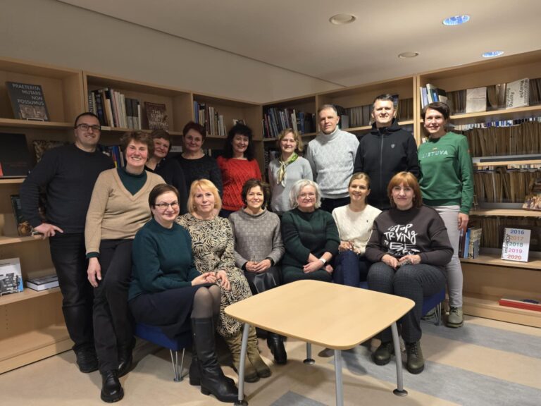 Angliškų pašnekesių klubo „Let's Talk“ grupė bibliotekos knygų lentynų aplinkoje