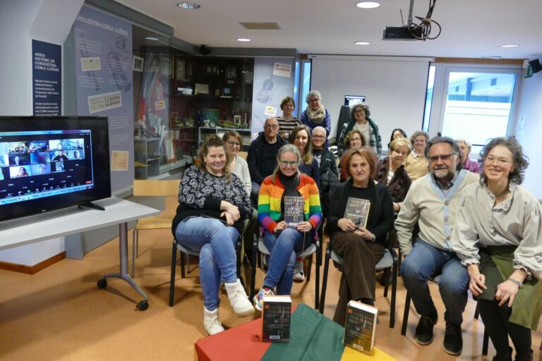 Grupė žmonių sėdi ir dauguma šypsosi bibliotekos salės erdvėje